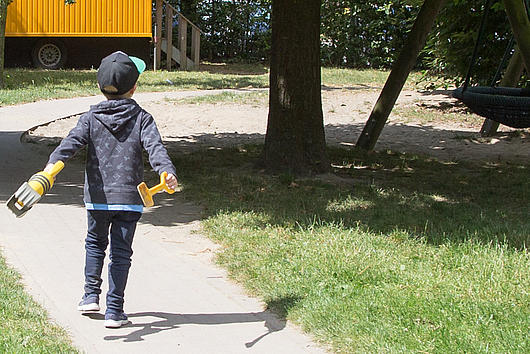Kindergartenkind mit Schaufel läuft auf Bauwagen zu 