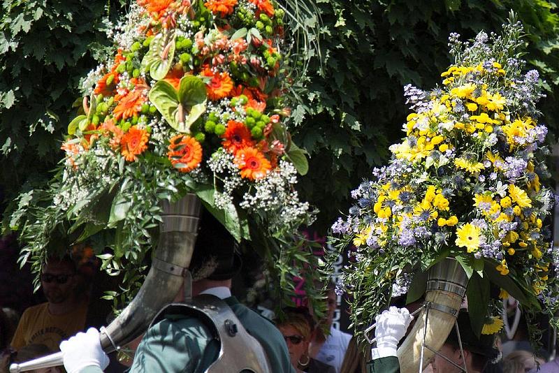 Ein Schützenfest-Umzug. Im Vordergrund tragen Personen Blasintrumente, die mit großen Blumengebinden bestückt sind.