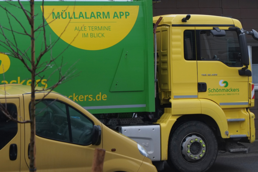 Müllwagen mit gelbem Schriftfeld fährt durch die Straße 