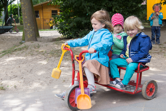 Drei Mädchen fahren auf einem Rollermobil durch das Außengelände der Kita Danziger Straße 