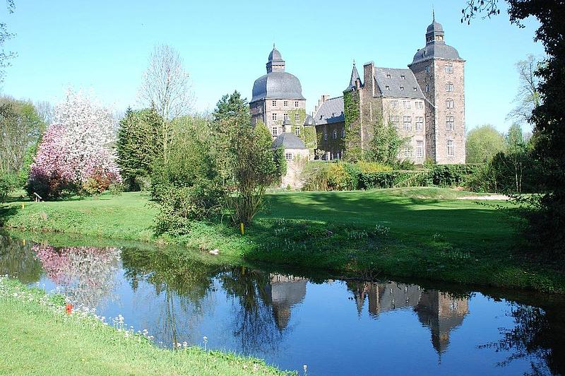 Schloss Myllendonk inmitten grüner Wiesen und umgeben von einem Wassergraben.